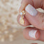 Close-up of a hand holding a gold teardrop charm stud earring with sparkling crystals and a round stud top.