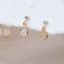 Close-up of dainty gold teardrop stud earrings with sparkling cubic zirconia, set against soft beige and white textured background.