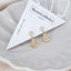 Elegant gold teardrop charm stud earrings with clear crystals, displayed on BenittaMoko jewelry card inside a ceramic dish.