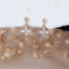 Gold flower stud earrings with marquise-cut cubic zirconia petals and round top stones, displayed on a soft neutral fabric background with dried floral accents.