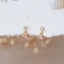 Delicate gold stud earrings with pink and clear round gemstones, displayed on soft fabric with dried flowers in the background.