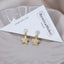 Pair of gold star charm stud earrings with crystal tops and pavé rhinestone stars, displayed on a BenittaMoko Jewelry card in a scalloped ceramic dish.