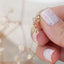 Small gold star charm stud earring with clear cubic zirconia, held between fingers to show size and sparkle detail