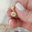 Close-up of a hand holding a gold sun charm stud earring with a clear crystal and eye detail in the center, showcasing intricate design and sparkle.