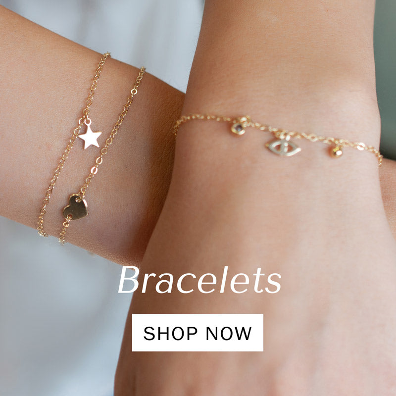 The image showcases the hands of a woman wearing three gold-colored bracelets. Each bracelet is adorned with small pendants including a heart, a star, an evil eye, and a zirconia charm. The bracelets add a touch of elegance and charm to the woman's wrists, reflecting her personal style and taste.