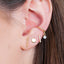 Image of a woman wearing four gold-colored earrings on her ear. The earrings are designed to fit together beautifully and include a bar stud earring, round dot earring, cz bar stud earring, and a white opal ear cuff. The combination of earrings creates a unique and fashionable look, suitable for various occasions