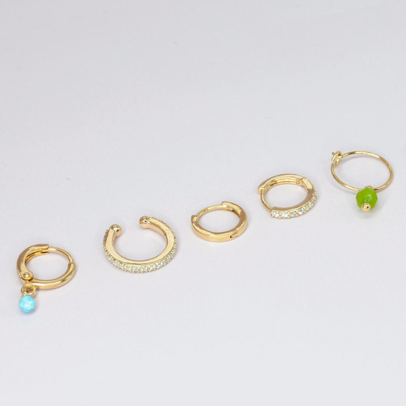 Five gold-plated earrings arranged diagonally. The earrings include cuffs and hoop earrings adorned with cubic zirconia and gemstones, adding a touch of elegance and sparkle to the accessories. The combination of the different designs and stones creates a unique and fashionable look, suitable for various occasions
