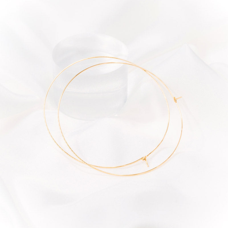Gold hoop earrings with a diameter of 3 inches resting on white silk fabric. The earrings are designed in a classic circular shape and feature a shiny, reflective surface. They are suitable for various occasions and add a stylish accessory to any outfit