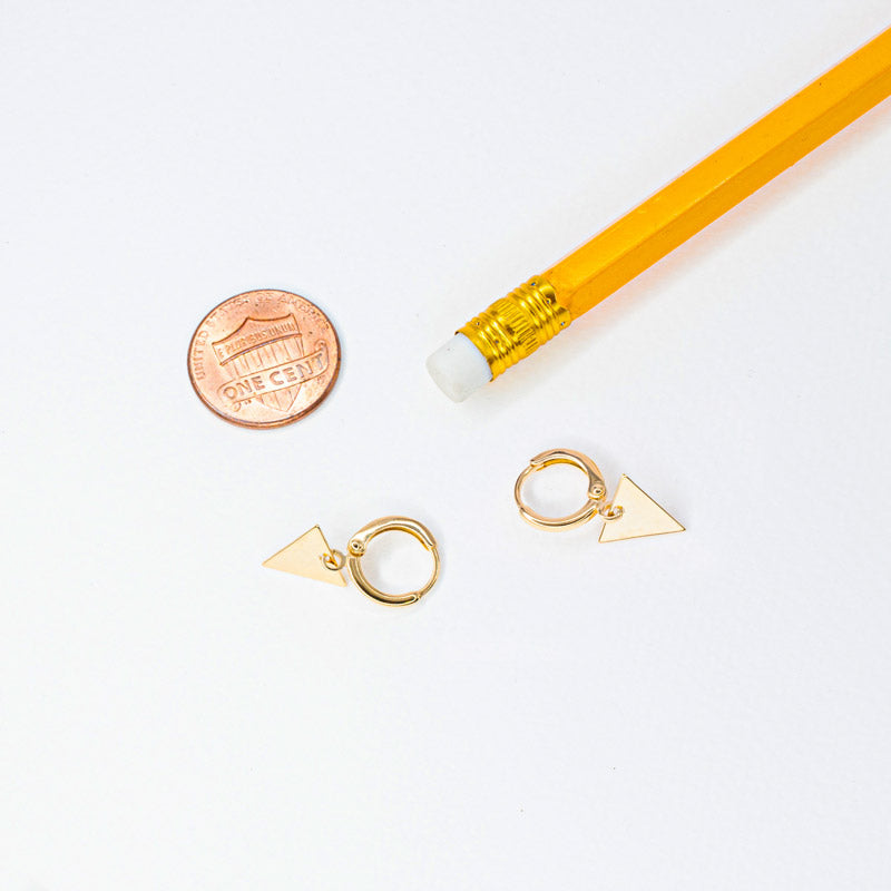A pair of gold hoop earrings lying next to a pencil and a 1 cent coin to provide a size reference for the earrings. The image allows viewers to better understand the size and scale of the earrings, making it easier to decide whether they are the right fit for their personal style and preference.